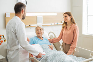 Woman and doctor support a senior in the hospital at her bedside